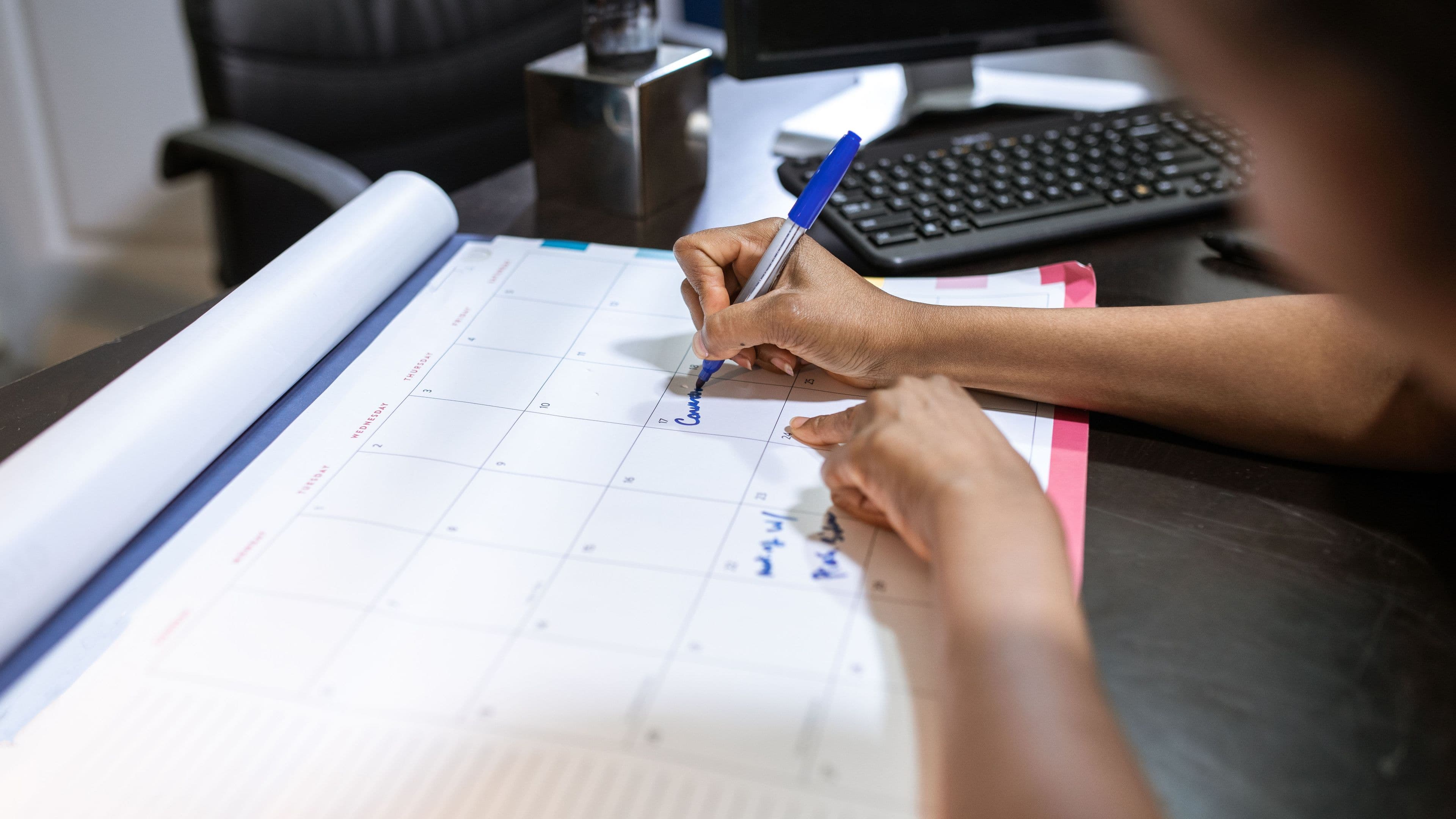 Hands marking dates on a large desk calendar
