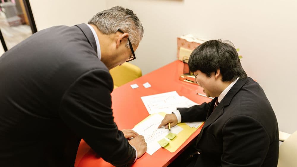 A senior colleague going through notes with a younger professional at a desk