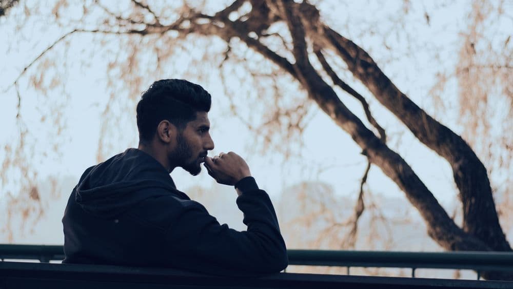 A man sitting outdoors in thought beneath bare branches