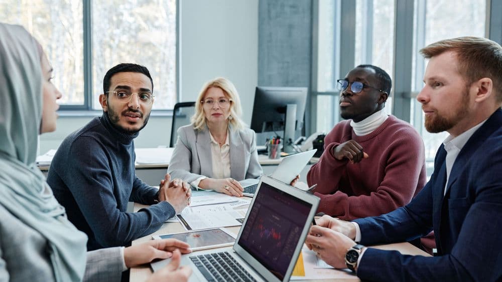A diverse team working through laptops and notes in a meeting room
