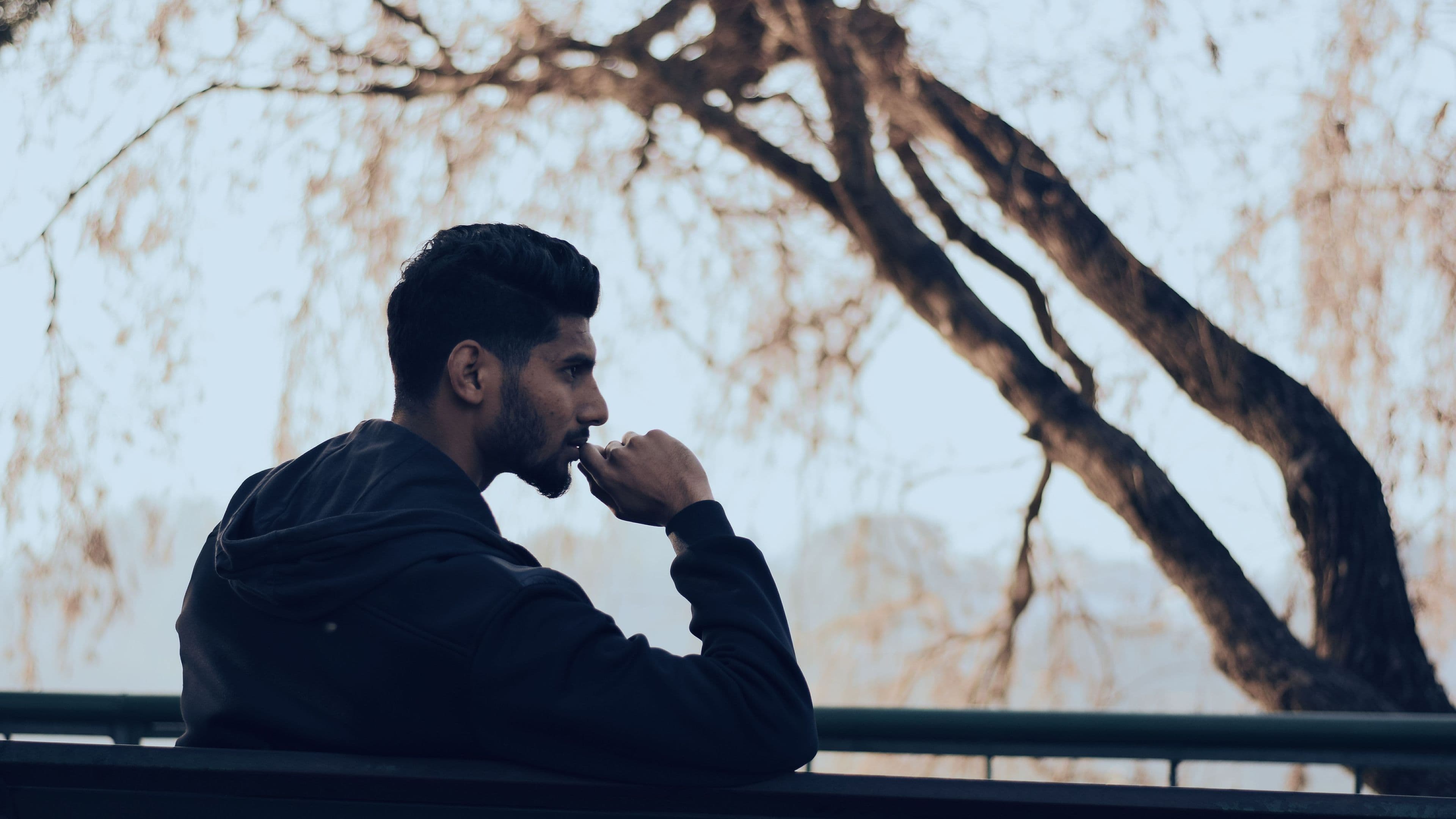 A man sitting outdoors in thought beneath bare branches