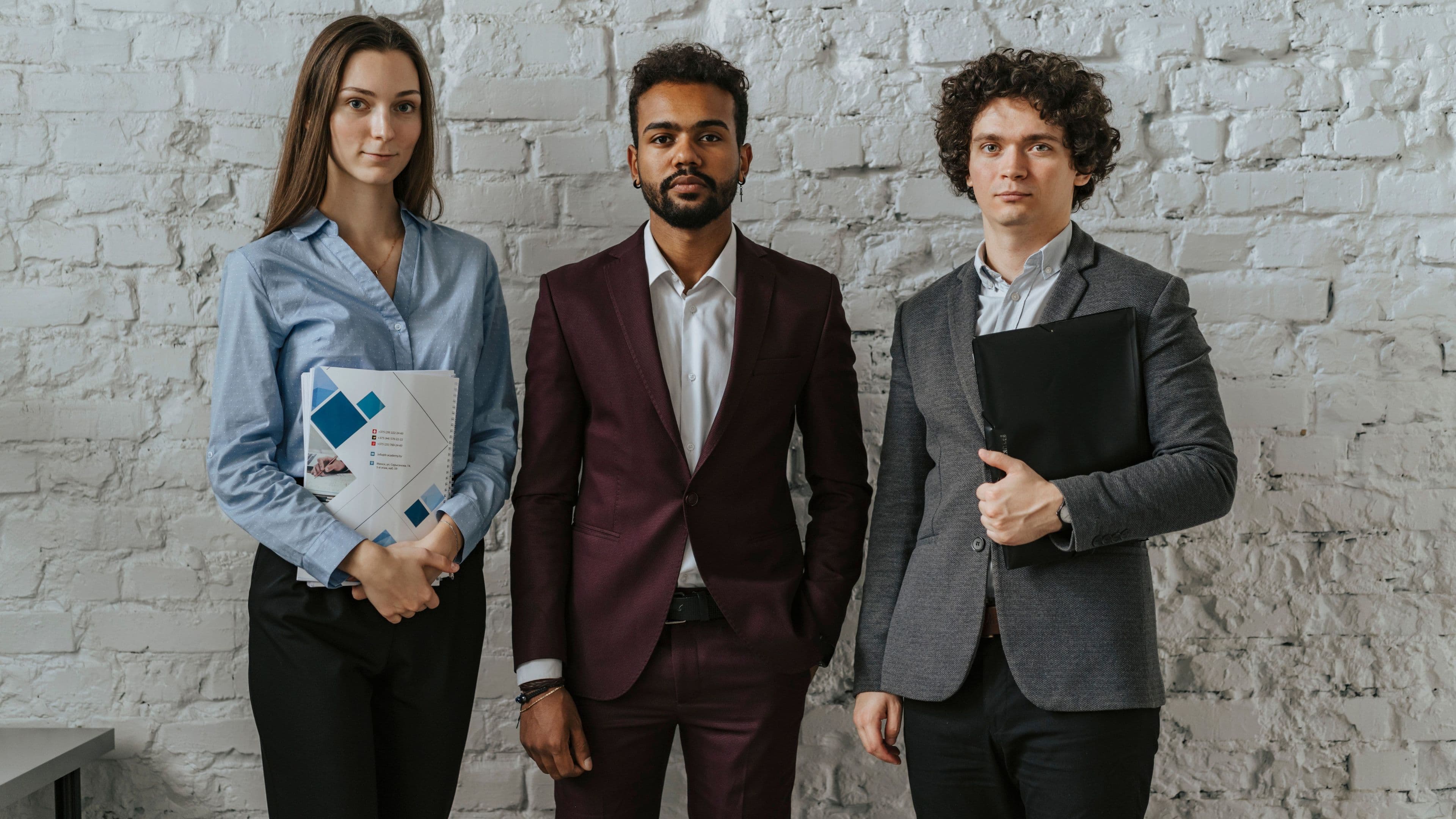 Three young professionals standing together against a brick wall